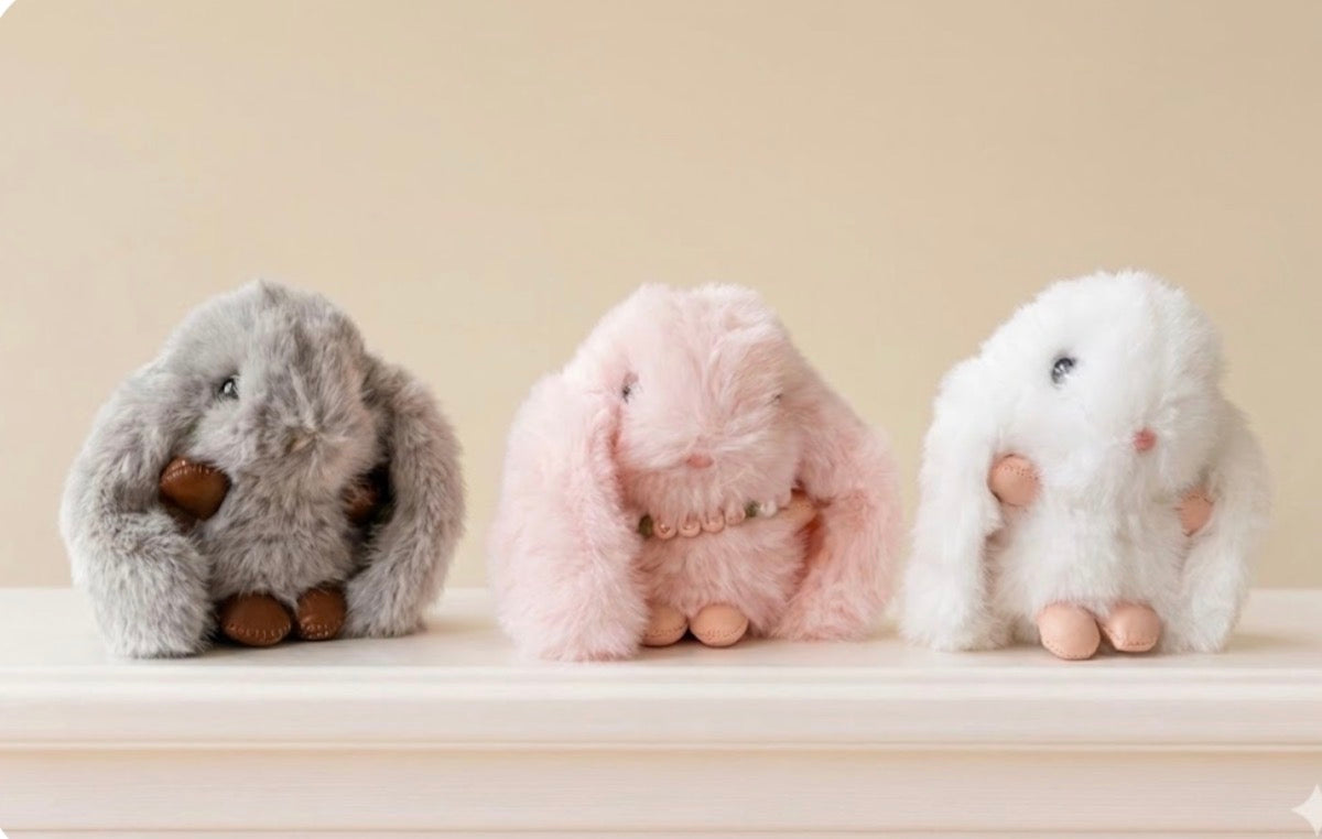 Three plush toys resembling bunnies on a light surface with a neutral background