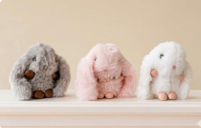 Three plush toys resembling bunnies on a light surface with a neutral background